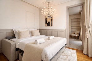 A bedroom with a bed, a chandelier, a painting, a chair, and a closet.