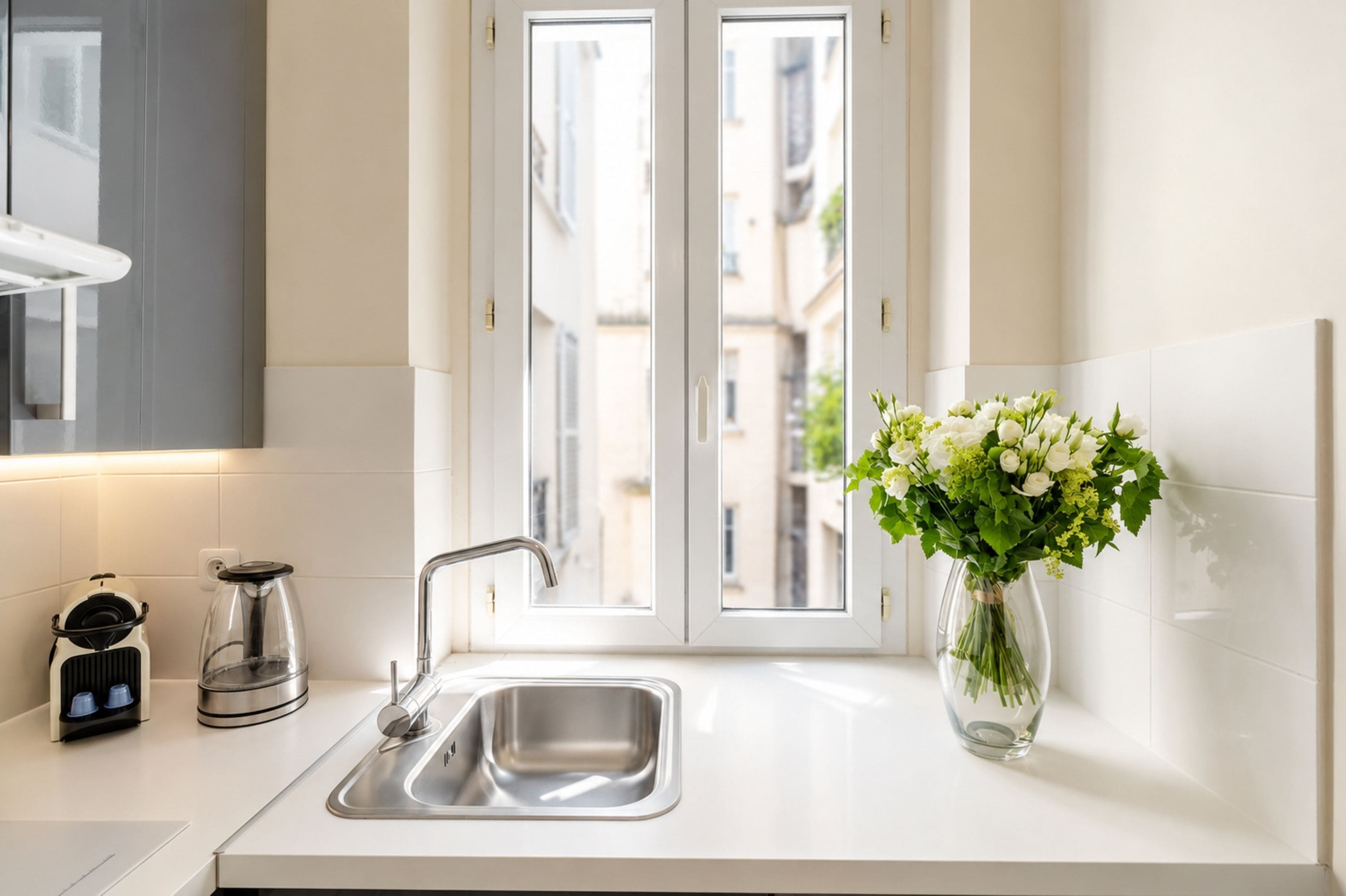 Una cocina moderna con un lavamanos de acero inoxidable, una cafetera y un florero con flores en la encimera.