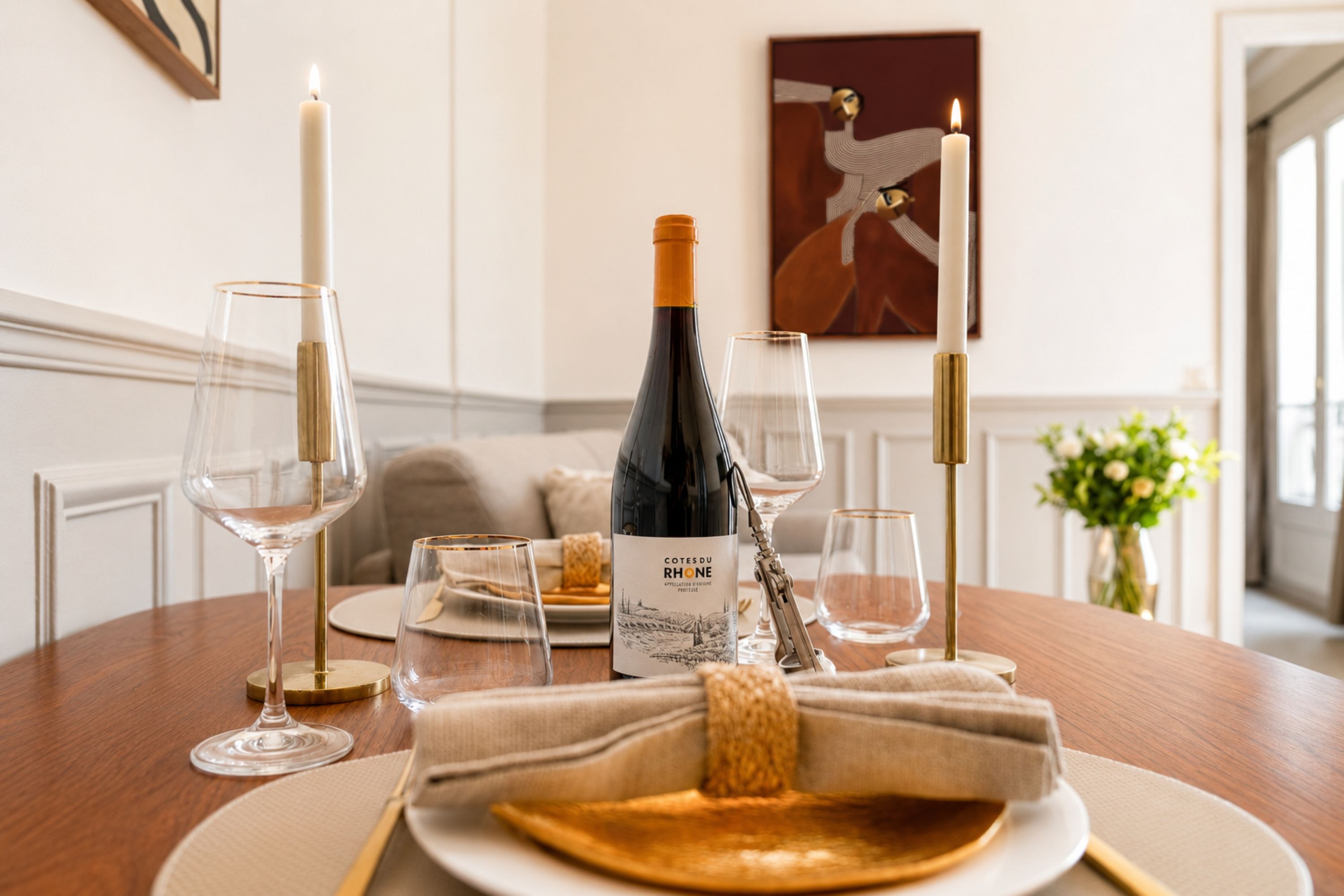 A dining table set with wine glasses, a bottle of wine, a candle, and a plate with a napkin.