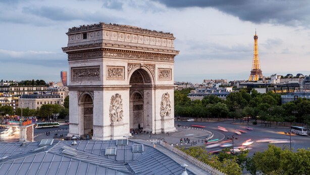 A large, historic arch structure with intricate carvings, surrounded by a busy urban area with modern buildings and a prominent tower in the background. - 1539 Belles Feuilles (Paris)