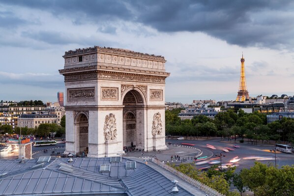 A large, historic arch structure with intricate carvings, surrounded by a busy urban area with modern buildings and a prominent tower in the background. - 1539 Belles Feuilles (Paris)