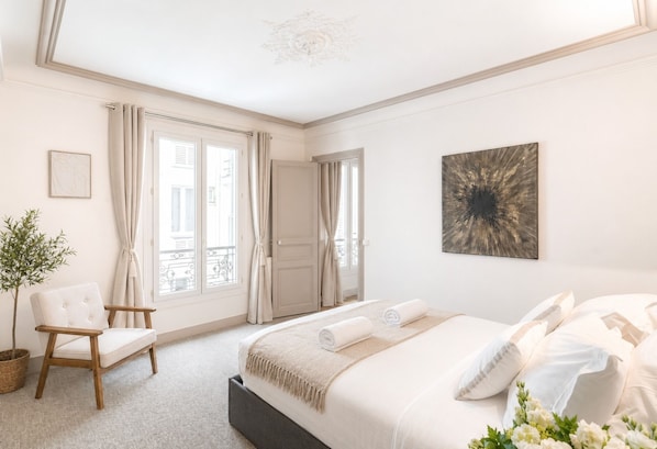 A bedroom with a bed, a chair, a potted plant, and a door leading to a balcony.