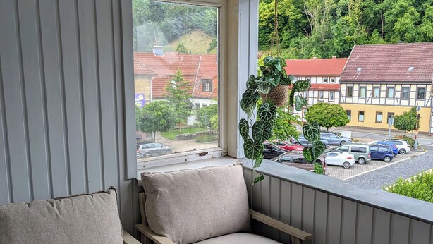 A balcony with two beige cushioned chairs, a hanging plant, and a view of a residential area with red-roofed houses. - A vacation with a view, a pleasant break in the heart of the city Dogs welcome (Bad Lauterberg)