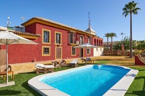 Ein rotes Gebäude mit Swimmingpool, Gartenmöbeln und Palmen.