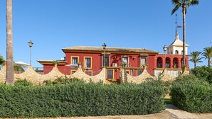 A red building with a white tower, surrounded by greenery and a clear blue sky.