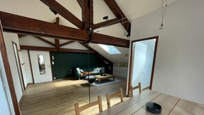 Un espacio amplio con techo alto, vigas de madera, una mesa de comedor y vistas a un salón con sofá y mesa de centro.