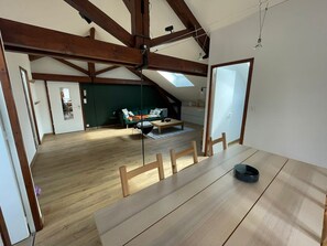 A spacious room with a high ceiling, wooden beams, a dining table, and a view of a living area with a sofa and a coffee table.