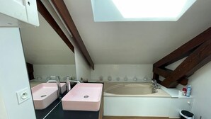 Un baño pequeño con tragaluz, bañera y dos lavamanos.
