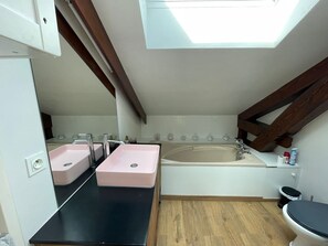 A compact bathroom with a skylight, a bathtub, and two sinks.