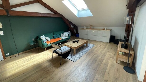 Una habitación estilo loft con techo inclinado, tragaluces, un sofá verde, una mesa de centro de madera y una mesita auxiliar pequeña.