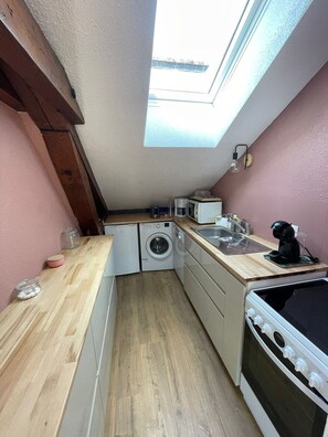 A compact kitchen with a skylight, a washing machine, a coffee maker, and a stove.