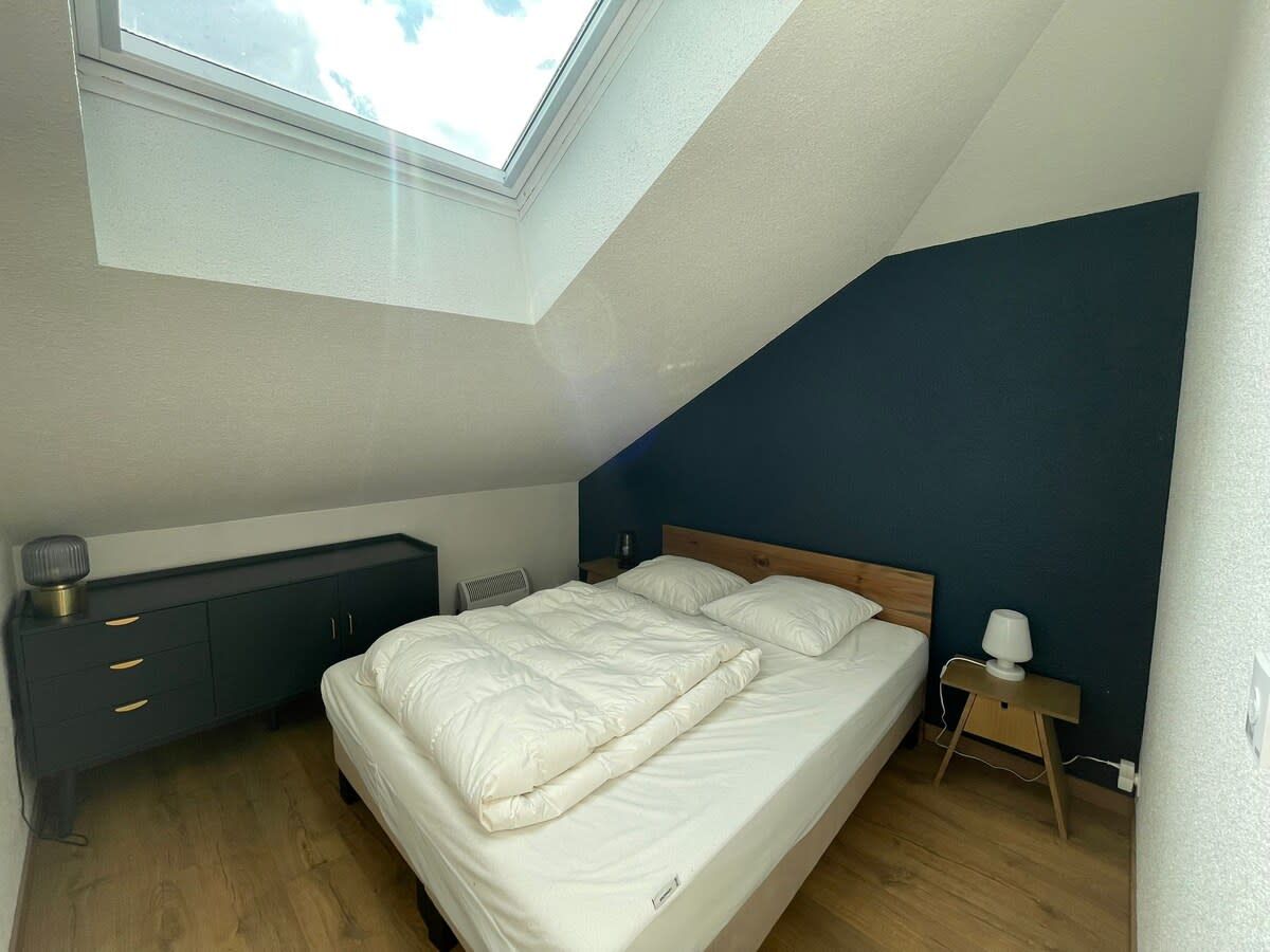 A bedroom with a skylight, a bed, a bedside table, and a dresser.