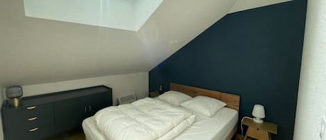 Une chambre à coucher avec un puits de lumière, un lit, une table de chevet et une commode.