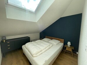 A bedroom with a skylight, a bed, a bedside table, and a dresser.