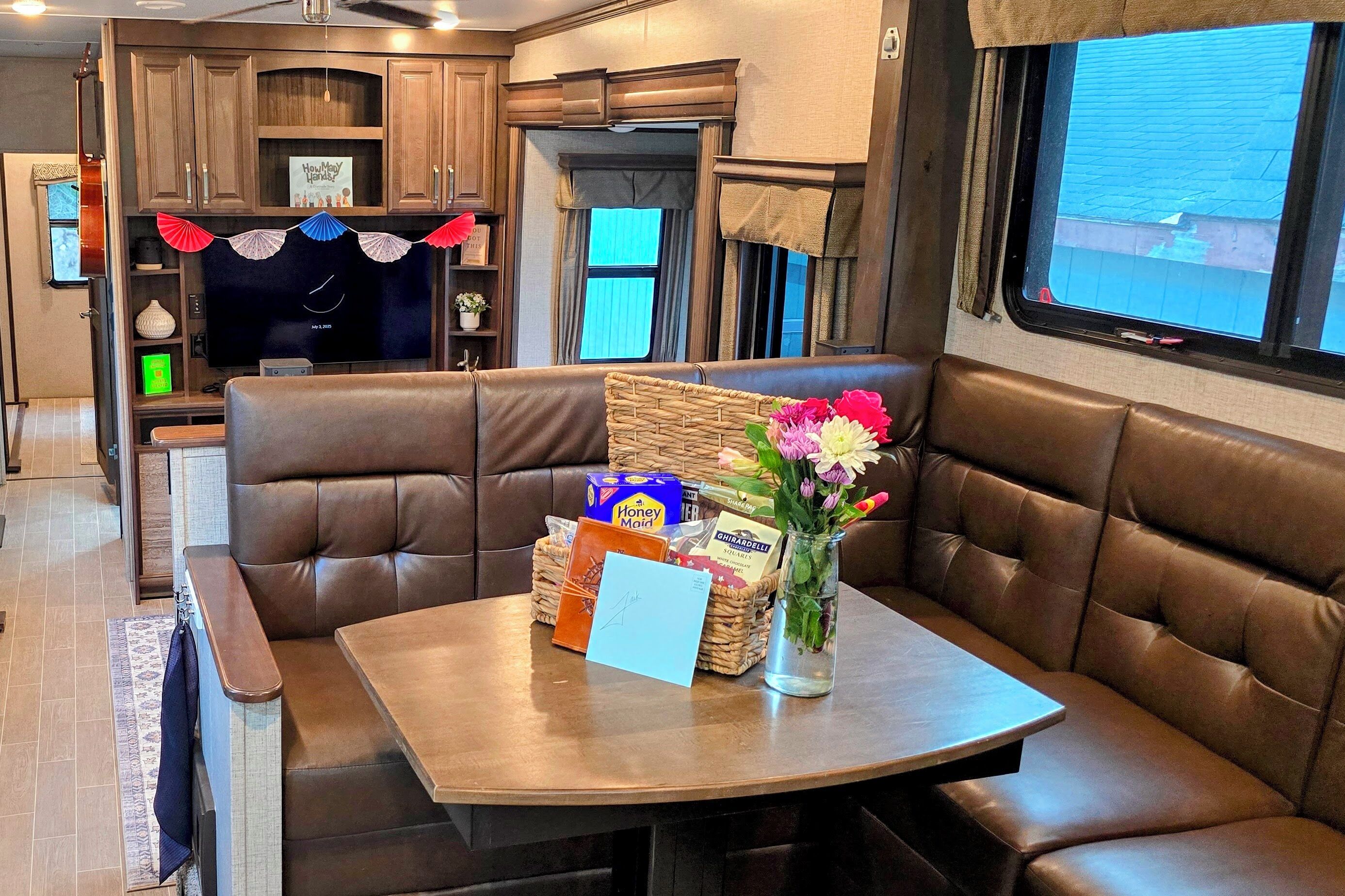 Interior acogedor de una caravana, con comedor que incluye una mesa, asientos acolchados y un florero con flores.