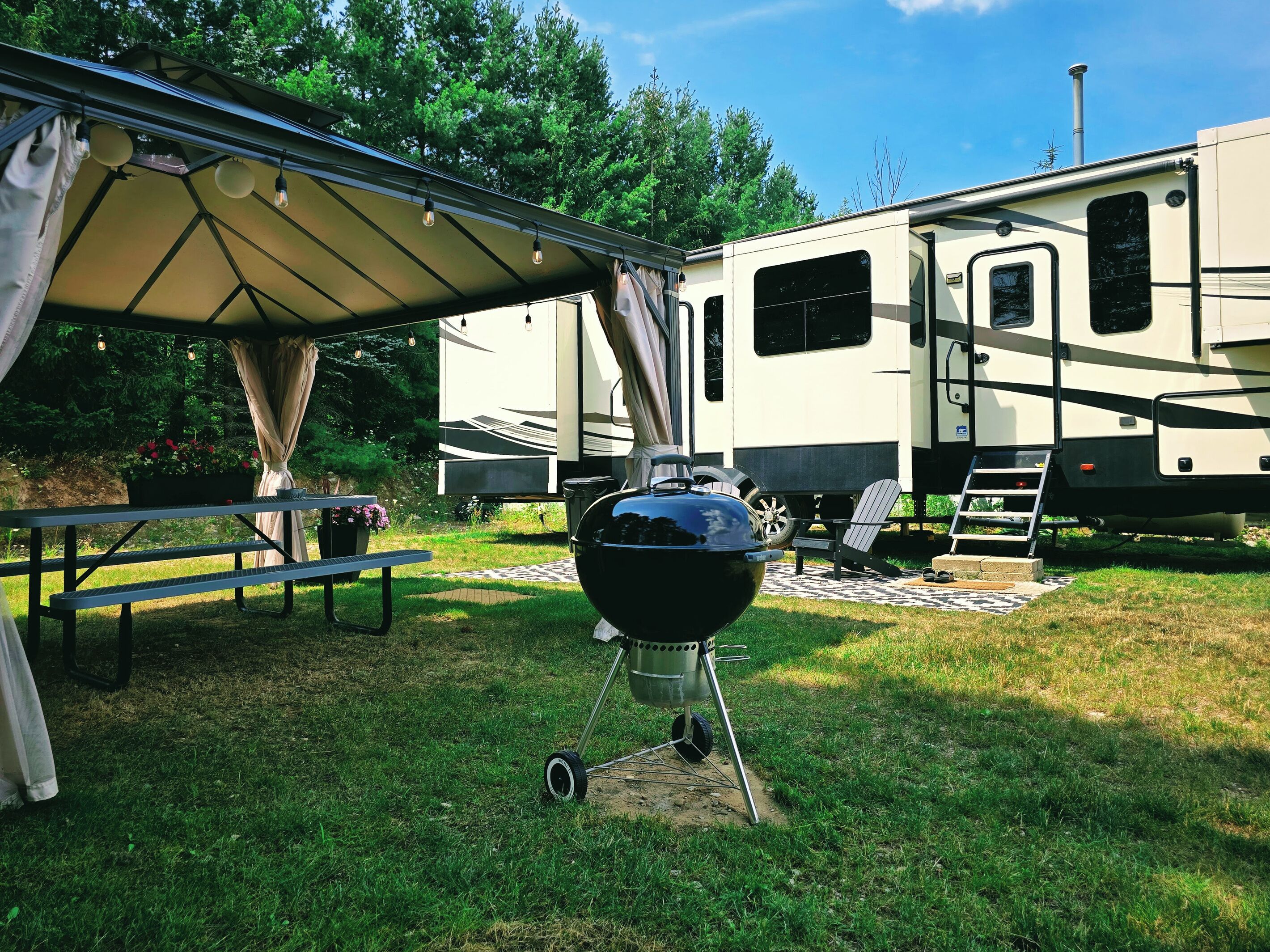 Un véhicule récréatif doté d’un patio couvert, d’un barbecue et d’une table de pique-nique.