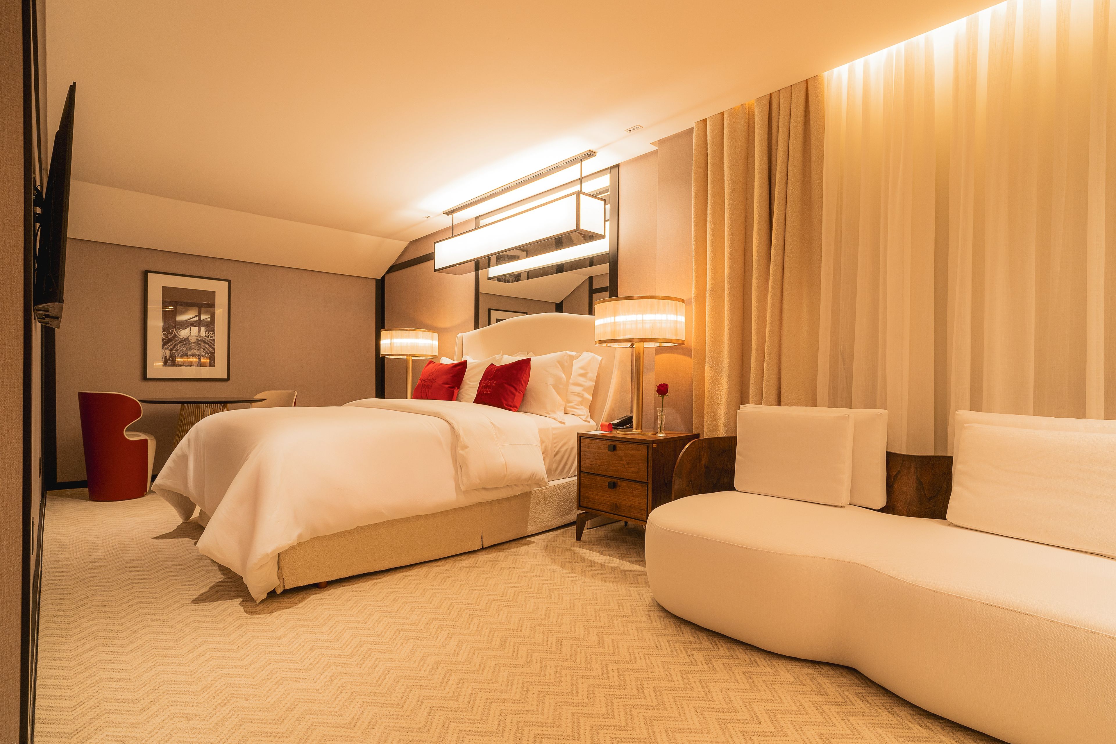 Habitación de hotel con una cama, mesitas de noche, una lámpara, un espejo y una silla roja.