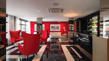 Un hall moderno con mobiliario rojo y blanco, piso de mármol y un ventanal grande.