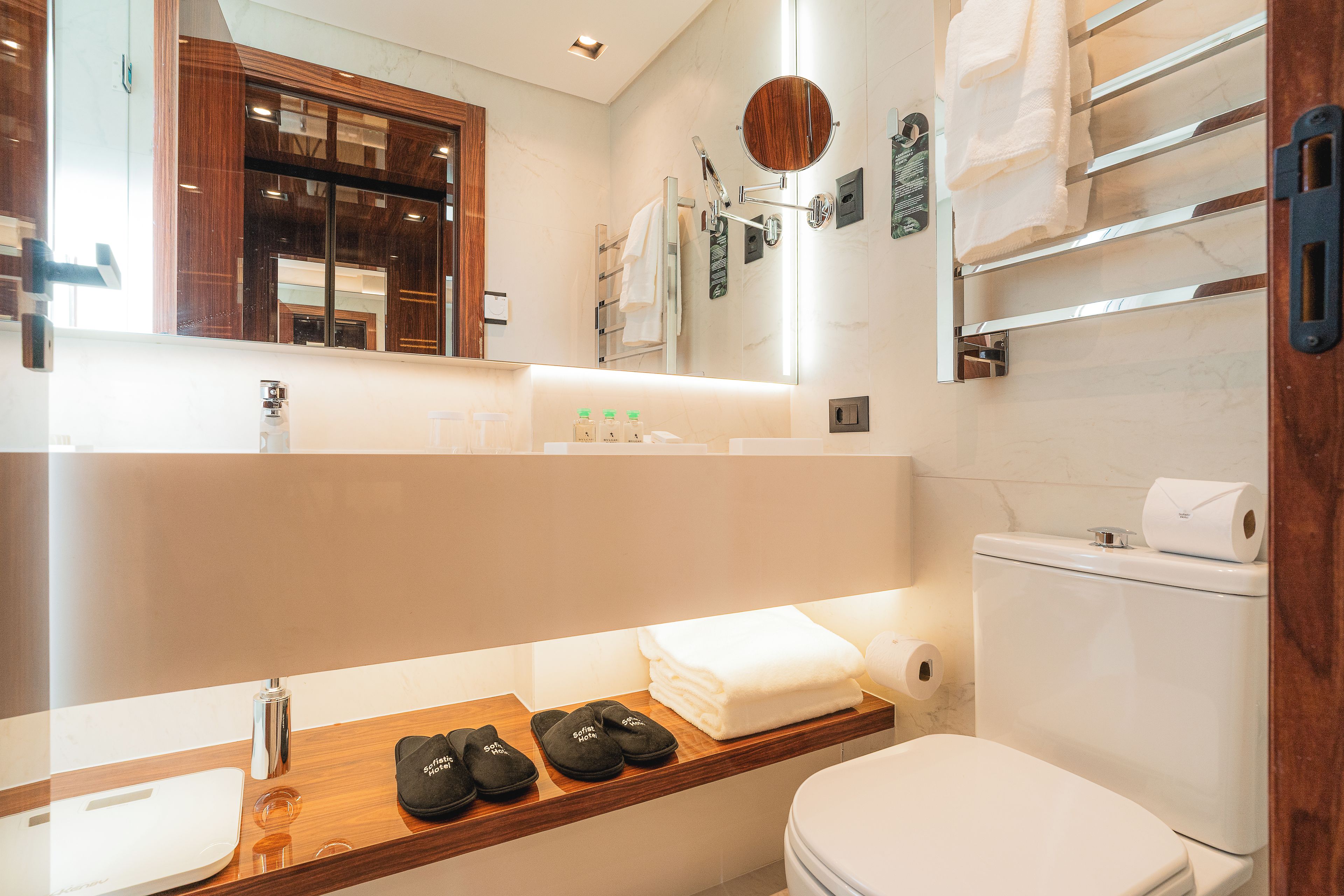 A modern bathroom with a vanity, a toilet, and a shelf with slippers.