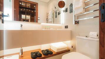 A modern bathroom with a vanity, a toilet, and a shelf with slippers.