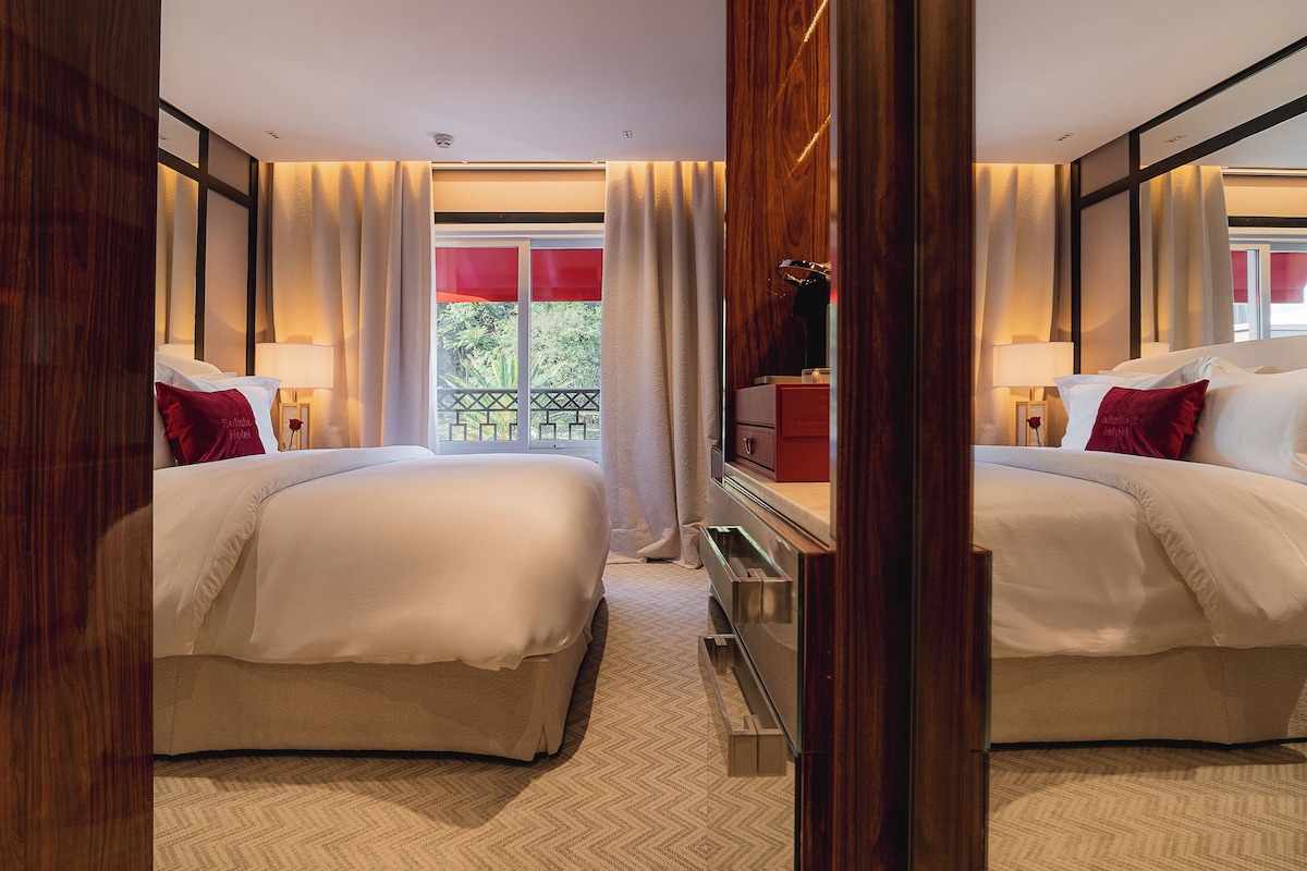 A hotel room with two beds, a dresser, a mirror, and a window with curtains.