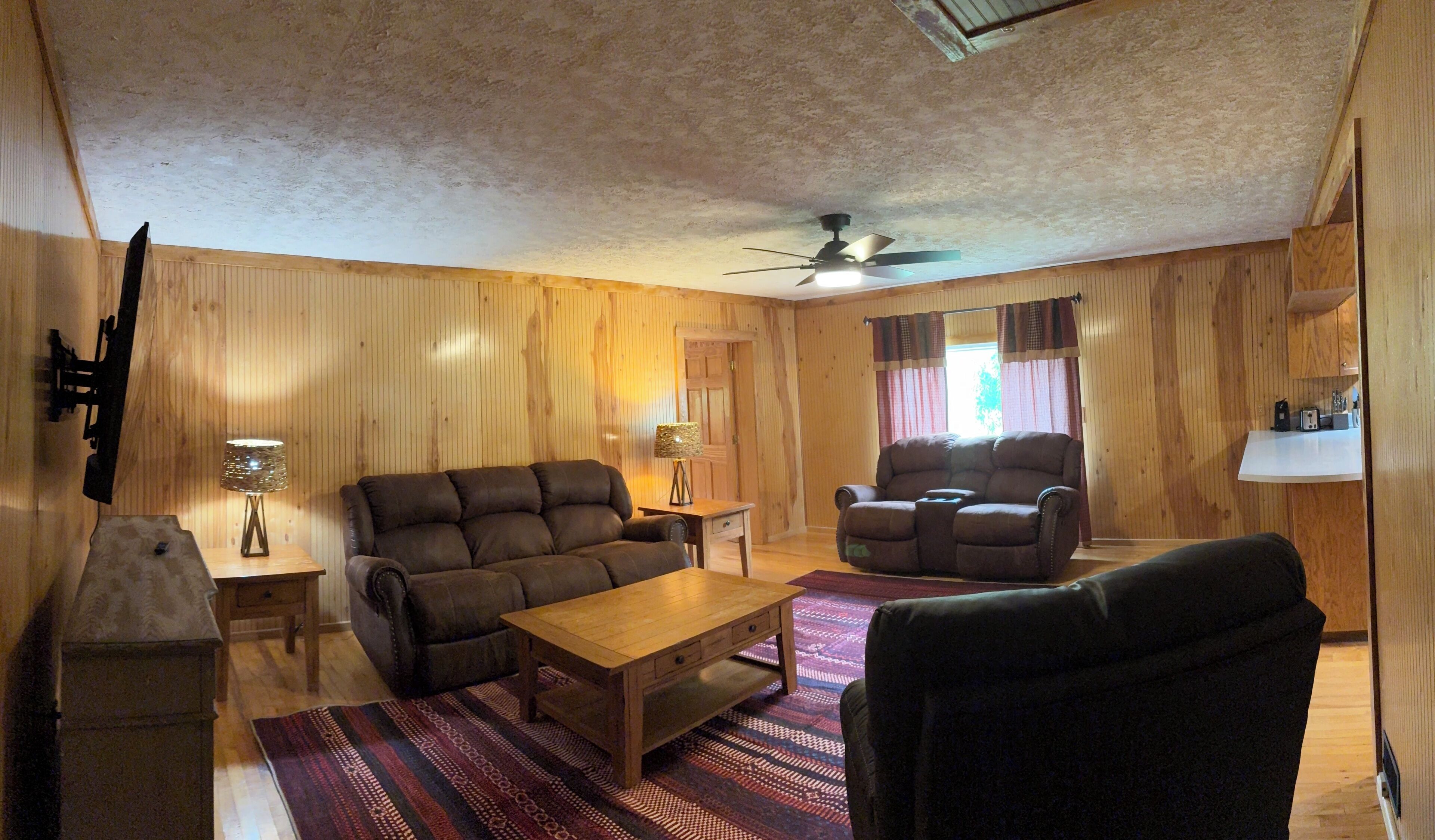 A cozy living room with a wooden ceiling, two sofas, a coffee table, and a ceiling fan.