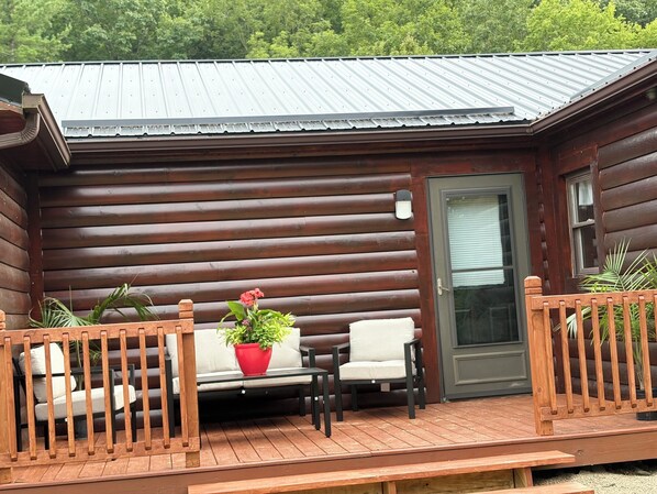 A log cabin with a deck, two chairs, a table, and a potted plant.
