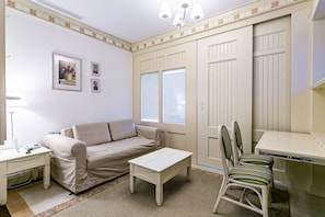 Una habitación con un sofá color crema, una mesa blanca, una silla a rayas y un escritorio blanco.
