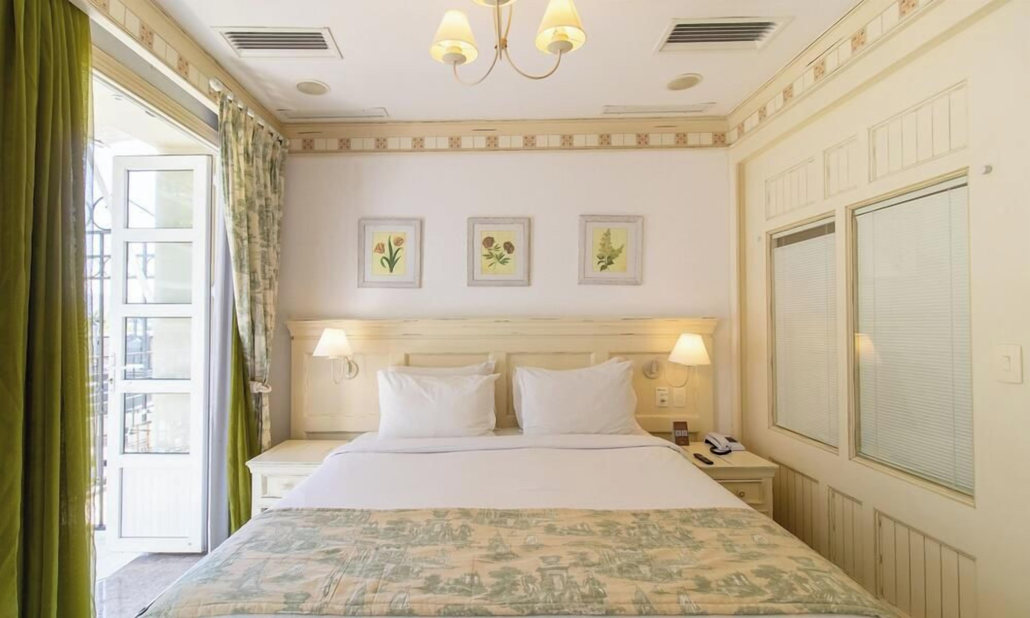 Una habitación de hotel con cama, dos mesitas de noche, una lámpara, teléfono y ventana con cortinas.