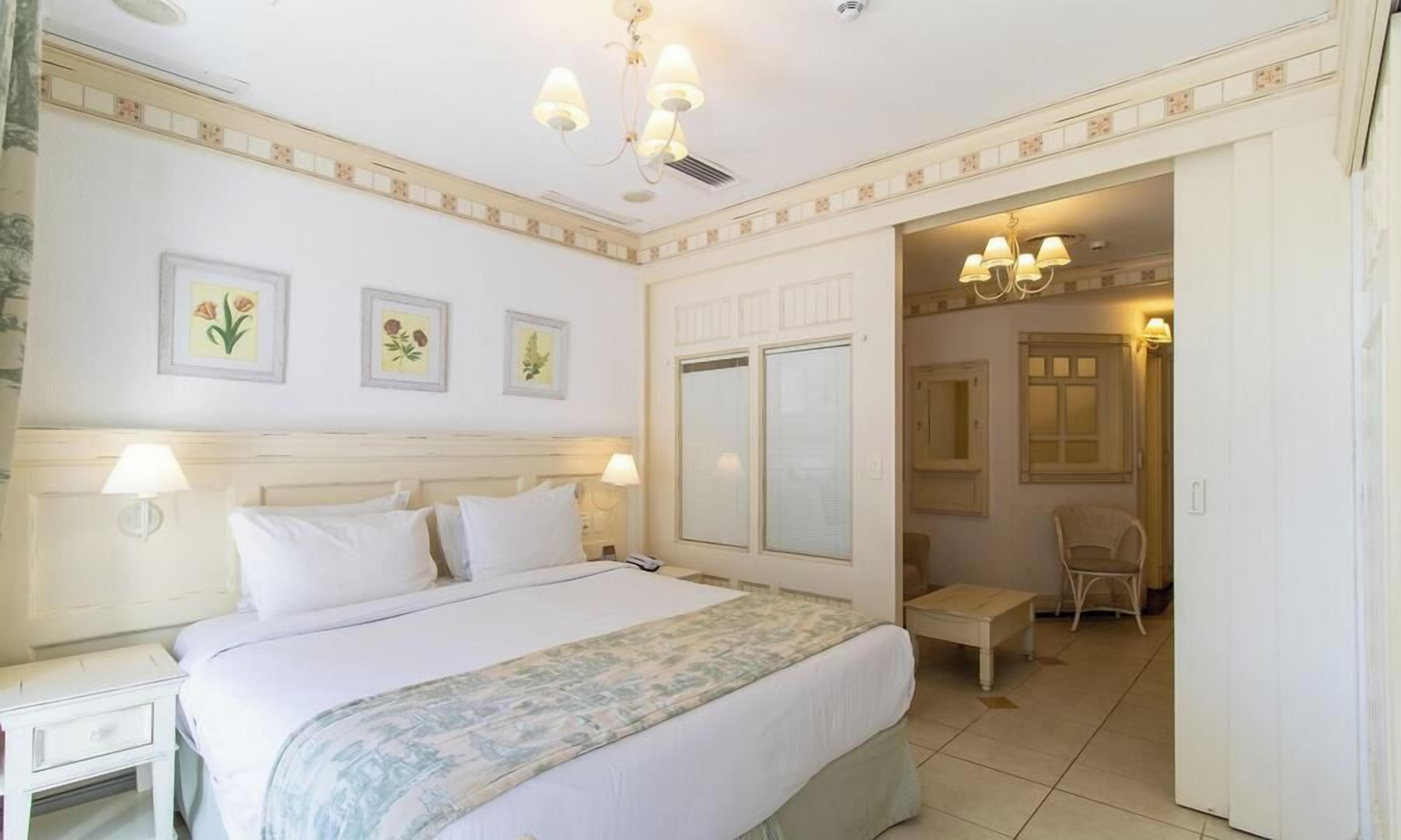 A hotel room with a bed, bedside tables, a chair, and a door leading to another room.