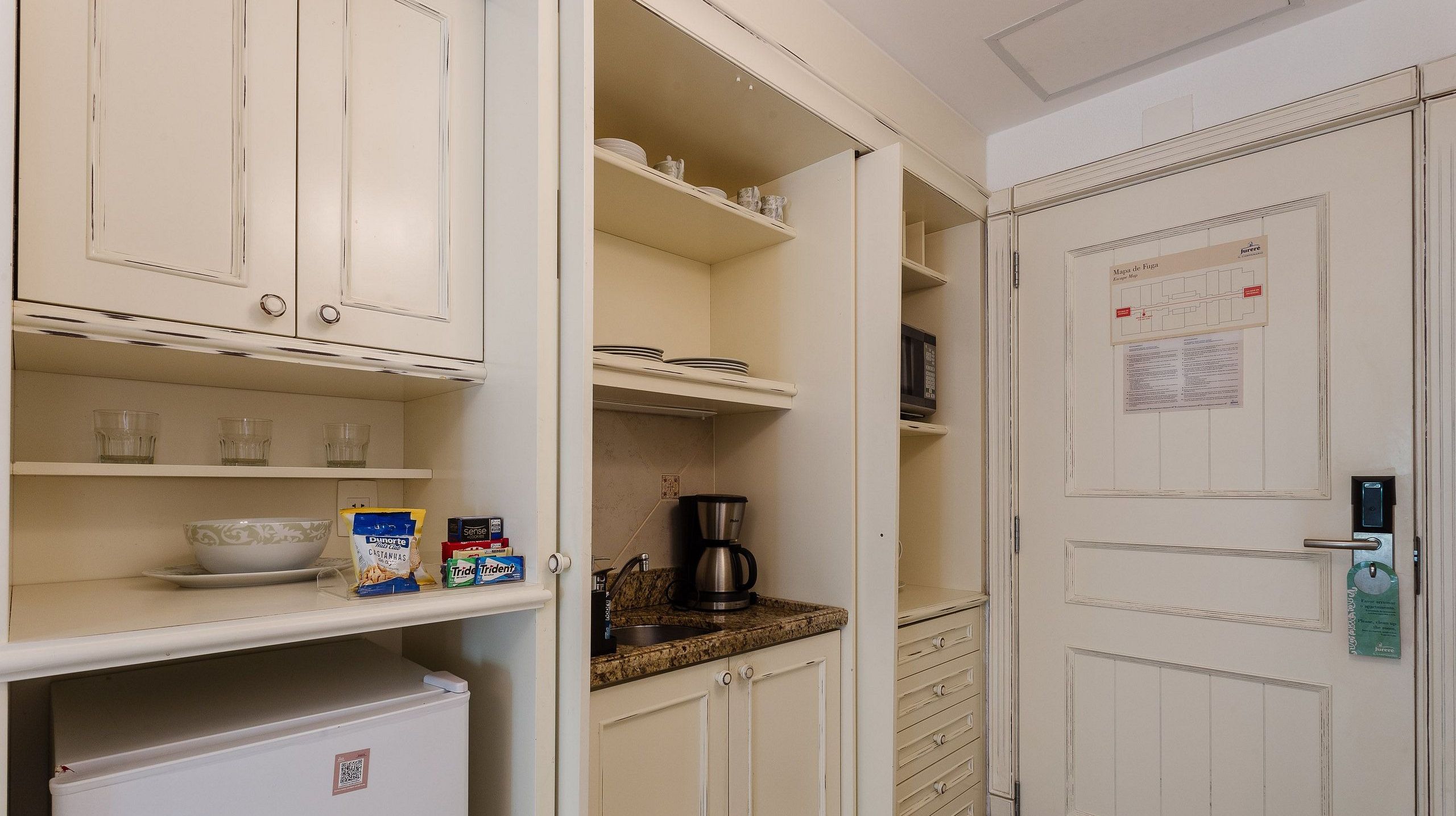 Eine Küche mit weißen Schränken, einem Kühlschrank, einer Kaffeemaschine und einer Mikrowelle.