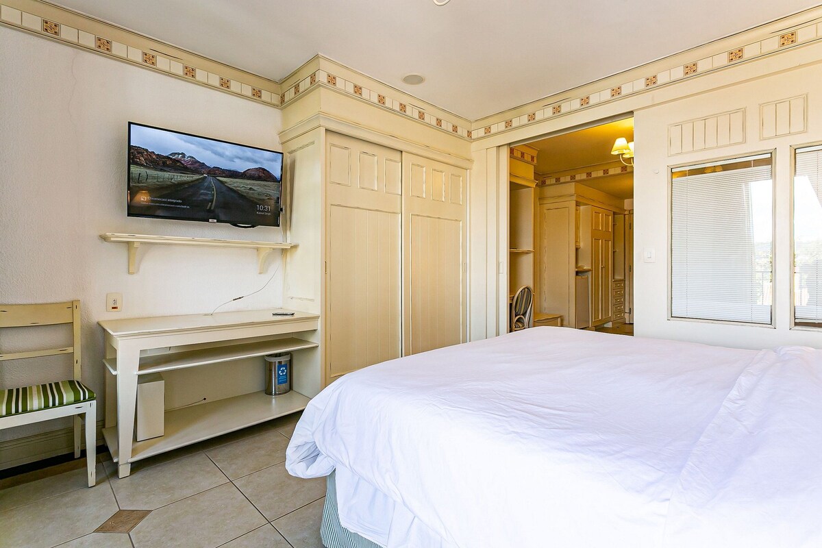 Quarto com cama, televisão na parede, escrivaninha e cadeira.