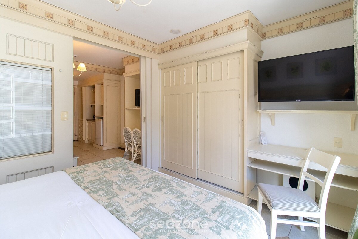 Quarto com cama, televisão na parede, escrivaninha e cadeira.