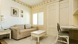 A room with a beige sofa, a small white table, a wicker chair, and a desk with a chair. There are pictures on the wall and a radiator on the wall. - Charmosos Studios no IL Campanario Villaggio Resort ILCJR II (Florianópolis)