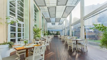 Un comedor interior con mesas y sillas, ventanas amplias y una terraza de madera.