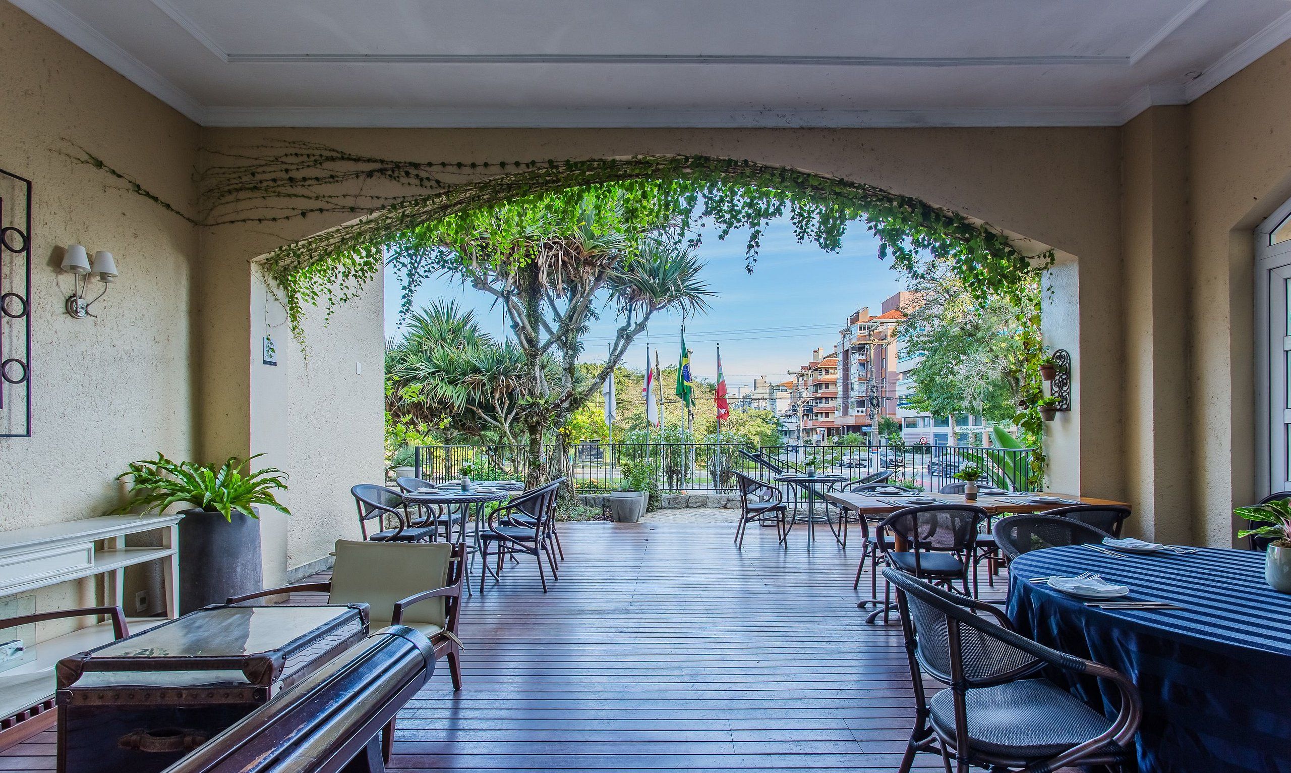 Un patio exterior con suelo de madera, mesas, sillas y plantas en macetas.
