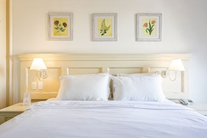 Quarto de hotel com uma cama grande, duas luminárias de cabeceira e três quadros florais na parede.