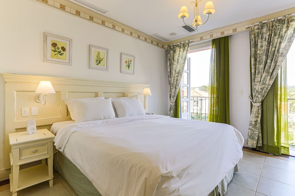 A neatly made bed with white linens, a bedside table with a lamp, and a wall-mounted telephone.