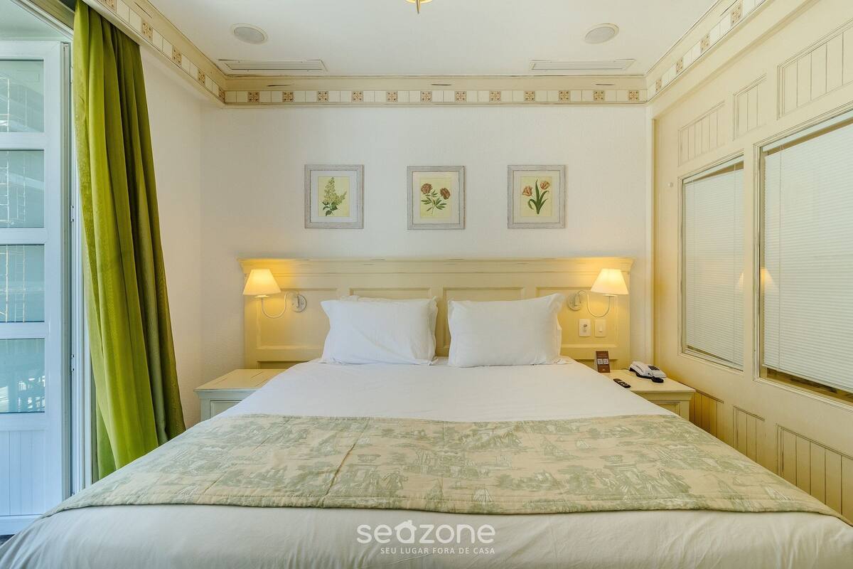 Habitación de hotel con una cama grande, dos lámparas de noche, una mesita de noche y un ventanal con cortinas.