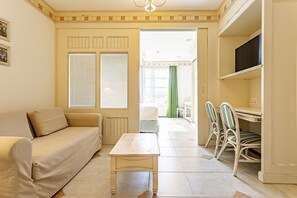 Una sala de estar con un sofá, una mesita y un escritorio con sillas. Hay una puerta que da a otra habitación.