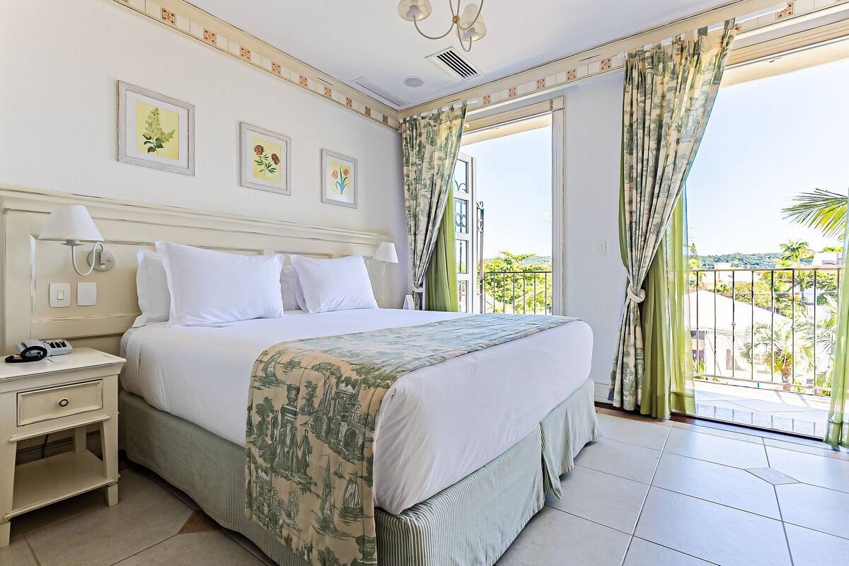 Habitación de hotel con una cama grande, una mesita de noche, un balcón con vistas a la ciudad y dos lámparas de pared.