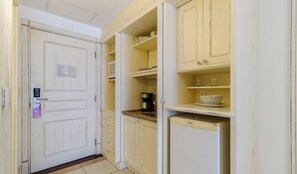 Una cocina estrecha con armarios blancos, una cafetera y un refrigerador.