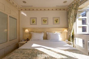 Quarto de hotel com uma cama, duas mesas de cabeceira, luminárias e três quadros florais na parede.