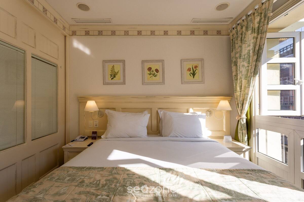 A hotel room with a bed, two bedside tables, lamps, and three framed floral pictures on the wall.