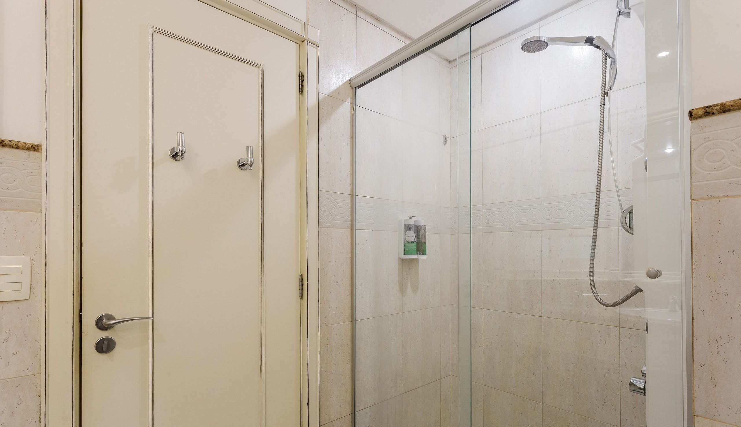 Une salle de bain avec une douche à parois de verre, une porte blanche dotée d’une poignée et une petite étagère contenant des articles de toilette.