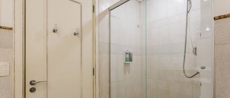 Une salle de bain avec une douche à parois de verre, une porte blanche dotée d’une poignée et une petite étagère contenant des articles de toilette.
