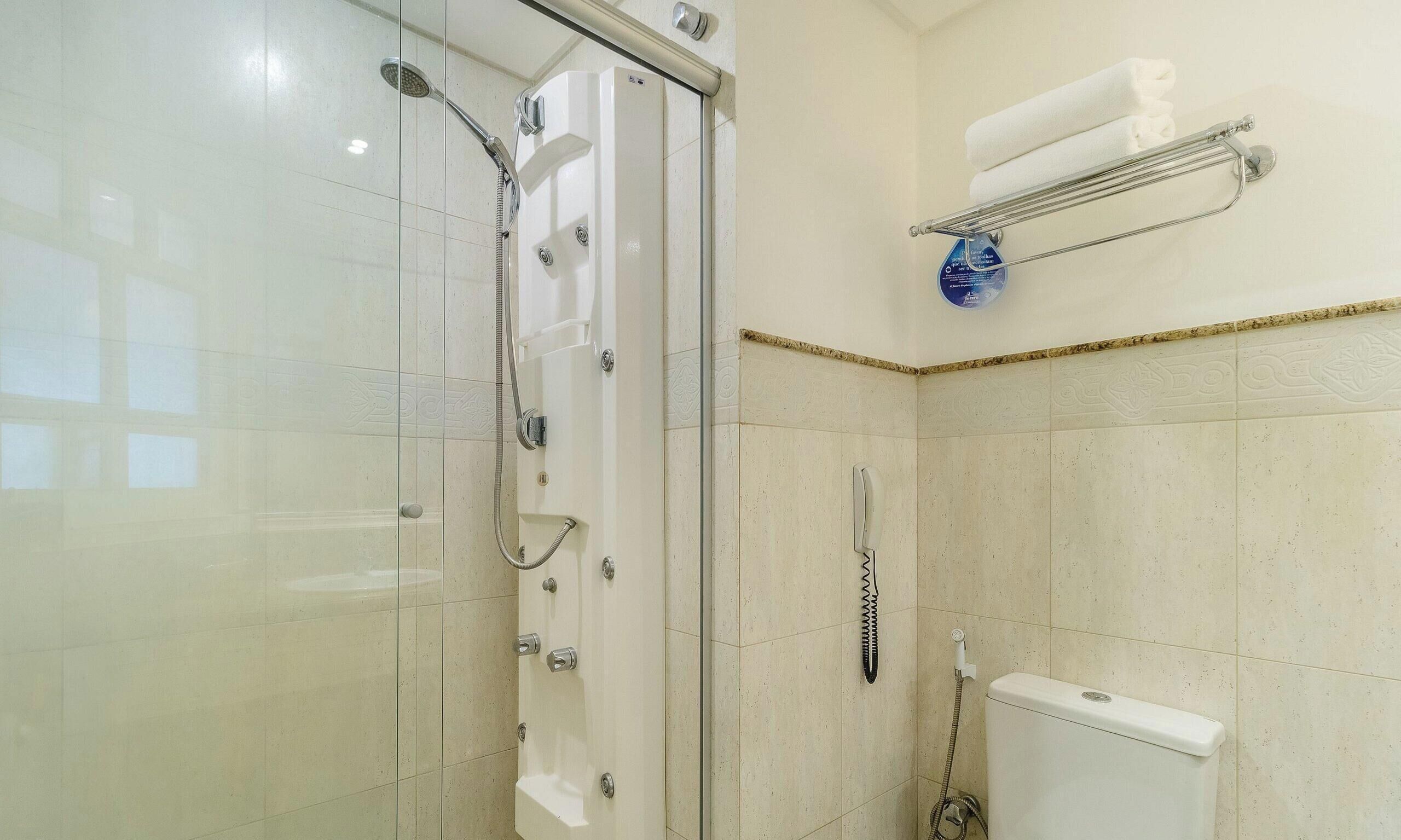 Un baño con ducha de vidrio, inodoro y toallero con una toalla doblada.