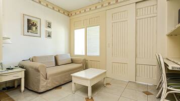 Een woonkamer met een beige bank, een witte salontafel en een eethoek met een witte stoel.