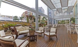Un patio interior amplio con suelo de madera, asientos acolchados blancos y grandes ventanales que ofrecen vistas de los edificios circundantes.