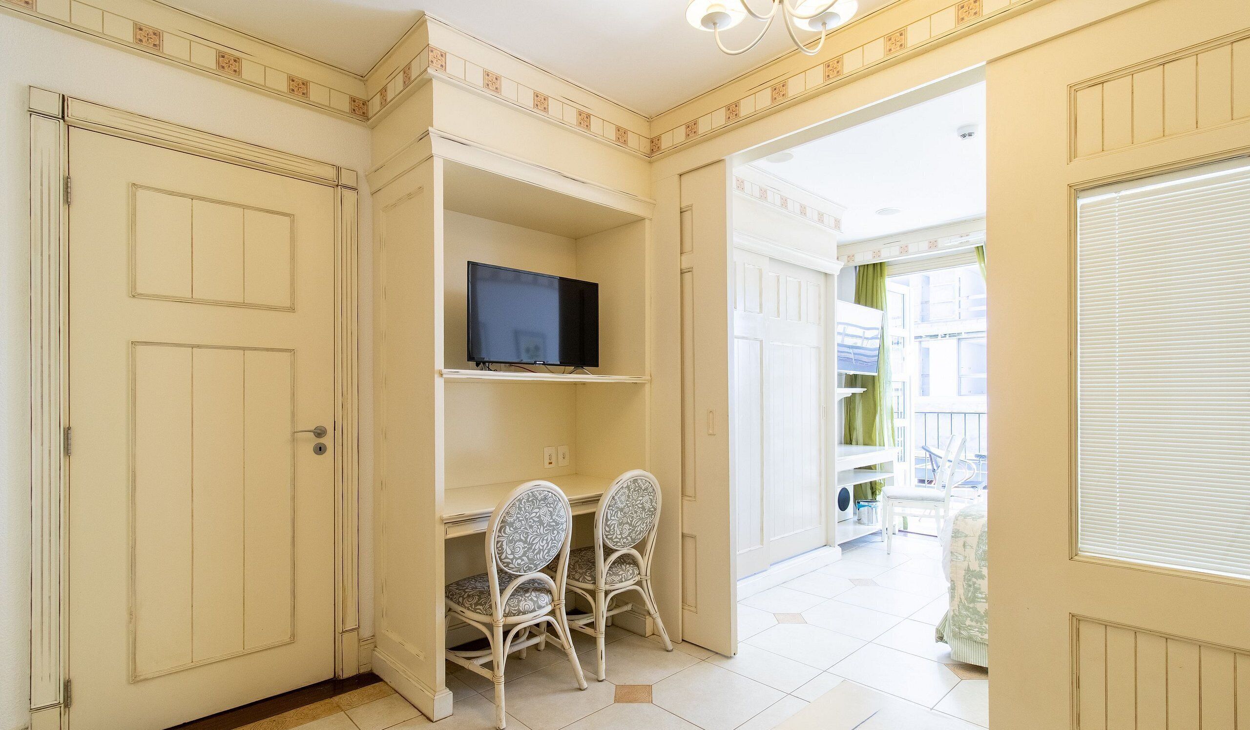 A room with a television on a shelf, two patterned chairs, and a door leading to a balcony with a view.